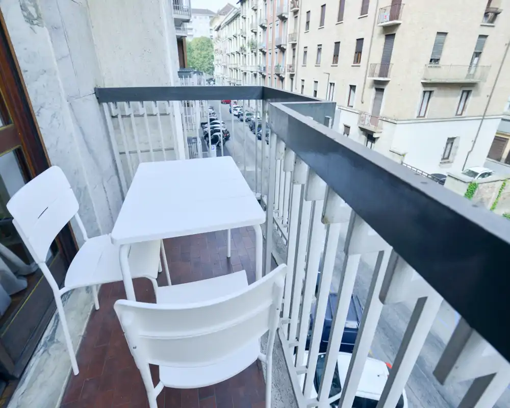 Balcón estrecho y soleado con una mesa blanca y tres sillas con vistas a una calle tranquila — ideal para el café de la mañana.
