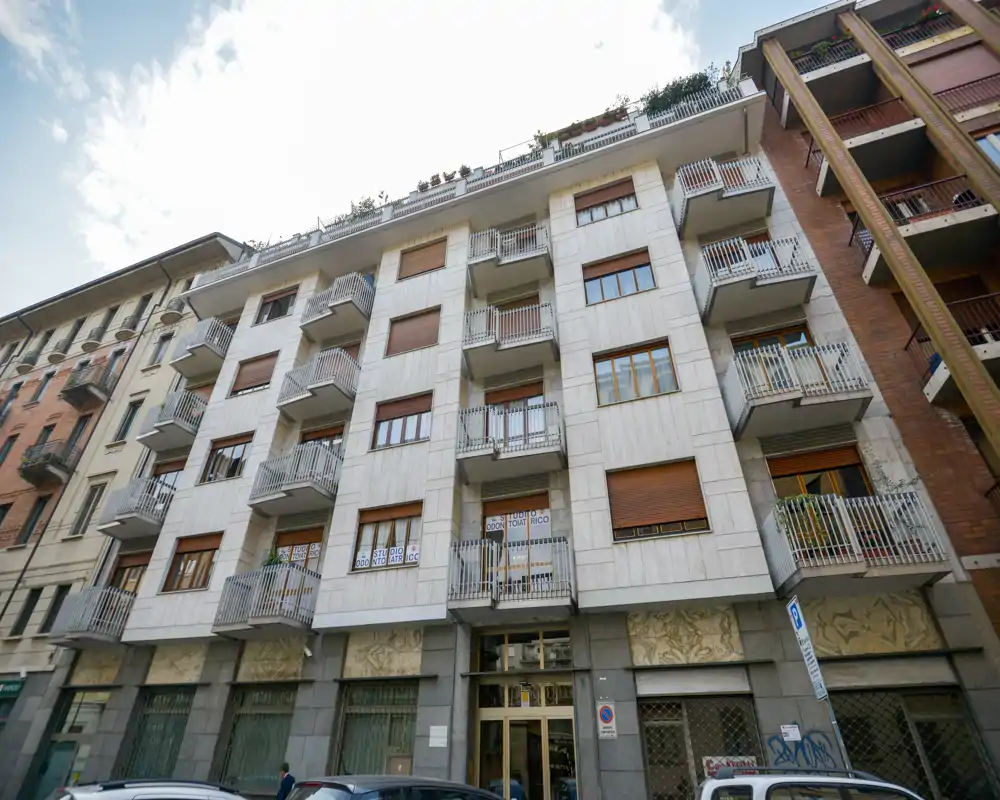 Fotografía exterior de la fachada de un edificio de apartamentos con varios balcones y la entrada en planta baja; la imagen muestra el exterior del edificio y no una habitación interior.