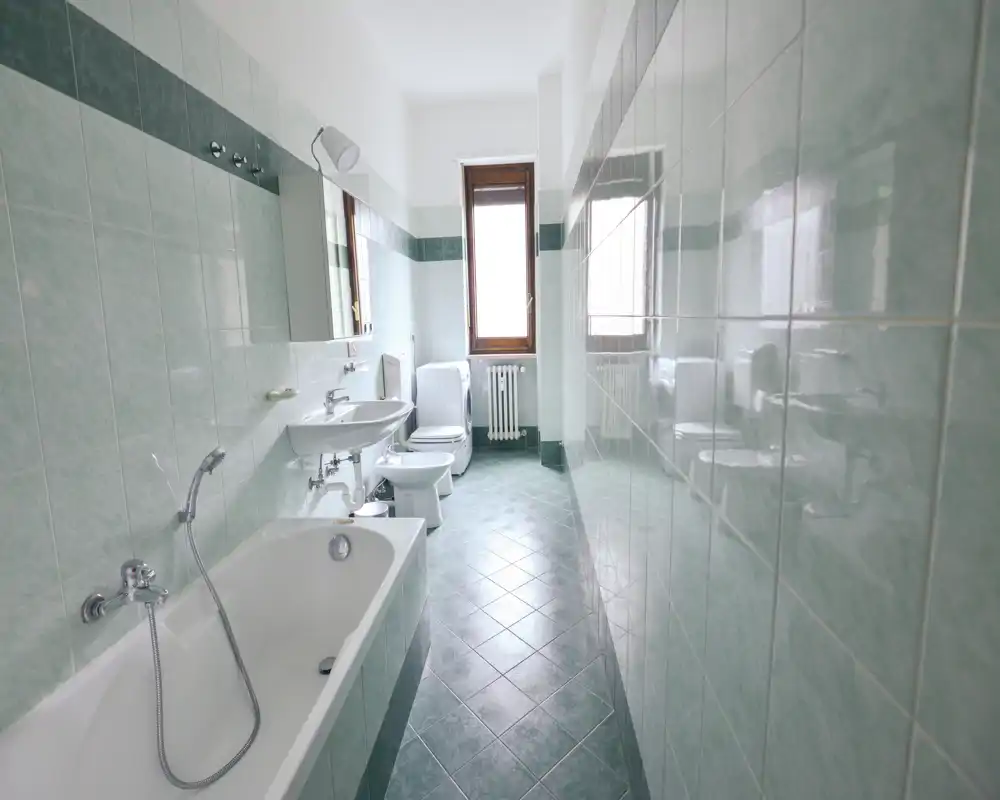 Baño alicatado y luminoso con bañera, lavabo, bidé, inodoro y una ventana que aporta luz natural; distribución larga y limpia.