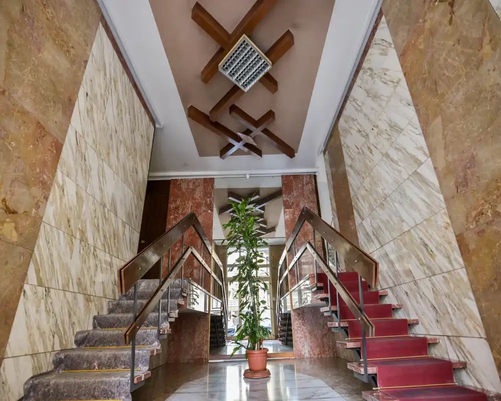 Amplia entrada con escaleras dobles simétricas, paredes y suelos de mármol y una planta central — recibidor elegante y bien iluminado.