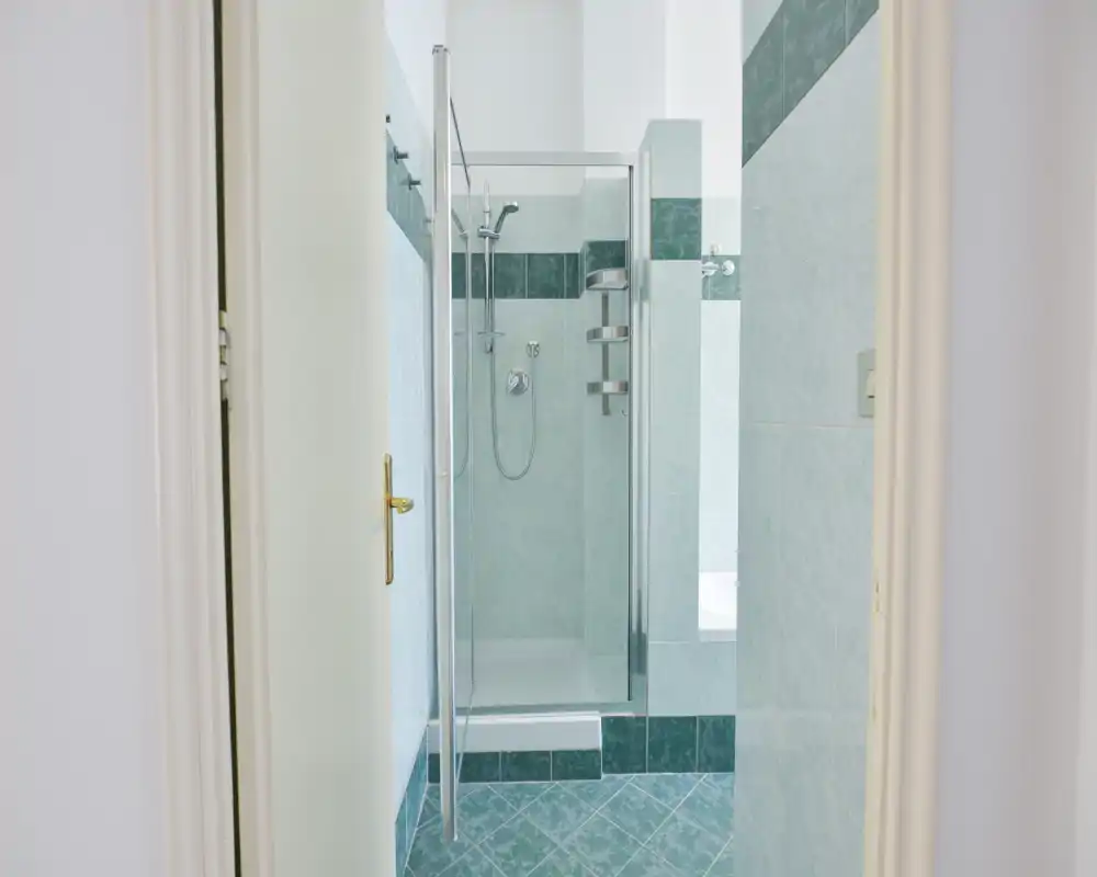 Baño luminoso y moderno con cabina de ducha de cristal, grifería cromada y azulejos verdes en paredes y suelo.