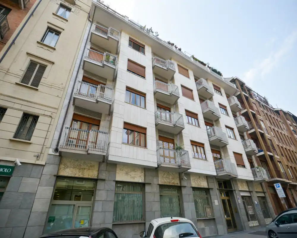 Vista exterior a nivel de calle de un edificio residencial de altura media con balcones y escaparates en planta baja; adecuada como foto de la fachada para un anuncio.
