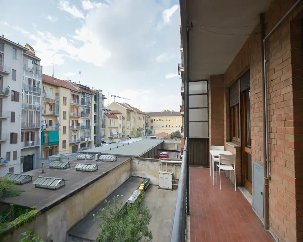 Balcón estrecho y soleado con vistas a un patio interior y edificios vecinos, amueblado con una pequeña mesa y sillas — ideal para el café de la mañana o un rincón exterior compacto.