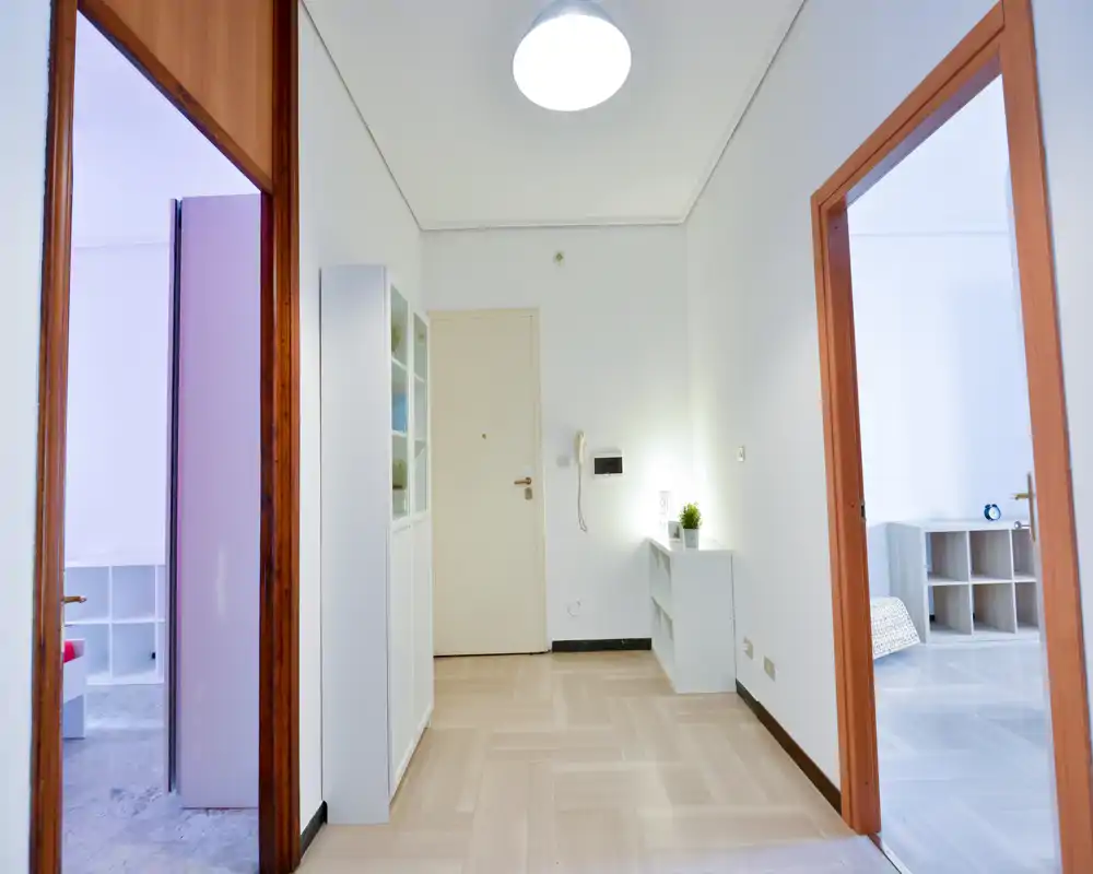 Entrada luminosa y minimalista con muebles de almacenamiento, portero y acceso a las habitaciones contiguas — líneas limpias y tonos neutros que ofrecen una primera impresión acogedora.