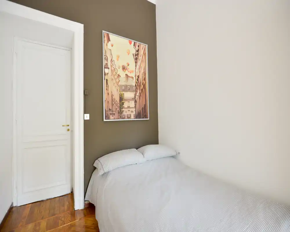 Camera da letto compatta con letto matrimoniale ben rifatto contro la parete, pavimento in legno caldo e una stampa incorniciata sopra la testata che dona un’atmosfera accogliente e minimal.