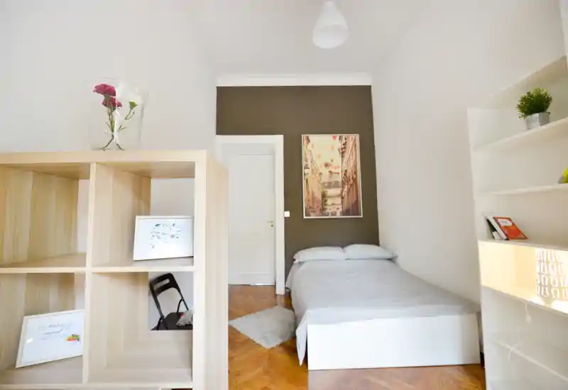 Camera da letto luminosa e compatta con letto matrimoniale ben rifatto contro una parete d'accento scura, parquet caldo e scaffalatura elegante che separa l'area notte.