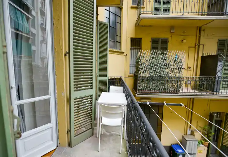 Piccolo balcone arredato che si affaccia su un cortile interno, con un tavolino compatto e sedie impilate — ideale per un caffè mattutino in città.