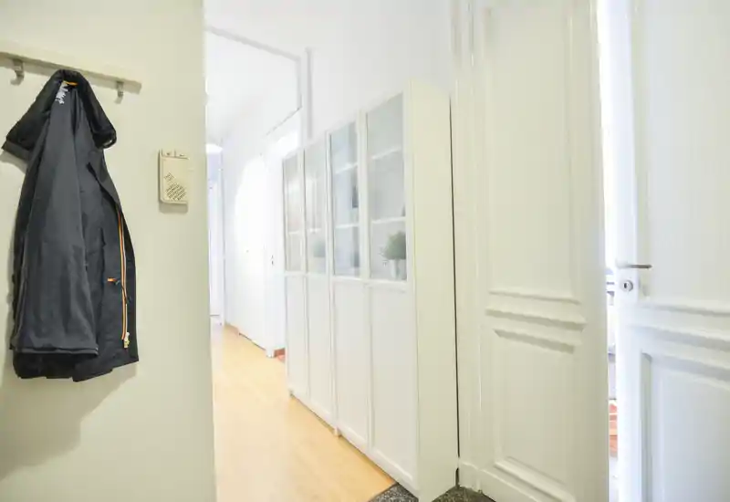 Ingresso luminoso e ordinato con appendiabiti a muro e mobile contenitore; pavimento in legno chiaro e porte bianche creano una sensazione accogliente.