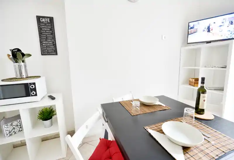 Angolo pranzo moderno e luminoso con tavolo nero apparecchiato per due, tovagliette in bambù e una bottiglia di vino—pulito, minimal e invitante.