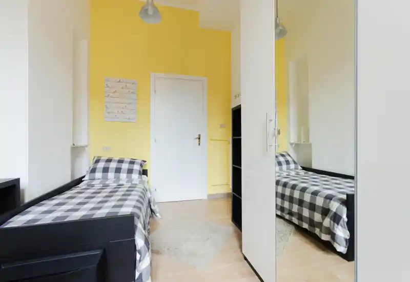 Chambre simple lumineuse avec lit à carreaux, sol en bois clair et armoire miroir qui agrandit l'espace visuel.