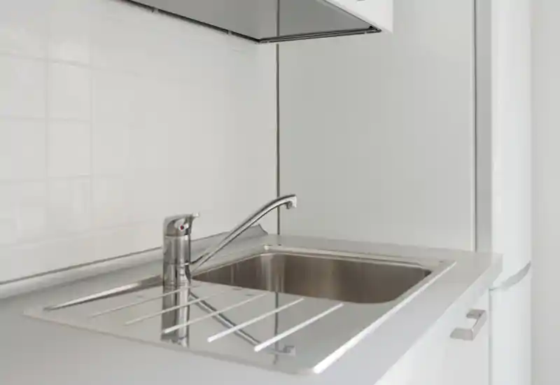 Angolo cucina moderno e luminoso con lavello in acciaio inox, rubinetto e paraschizzi piastrellato — minimal e ben tenuto.