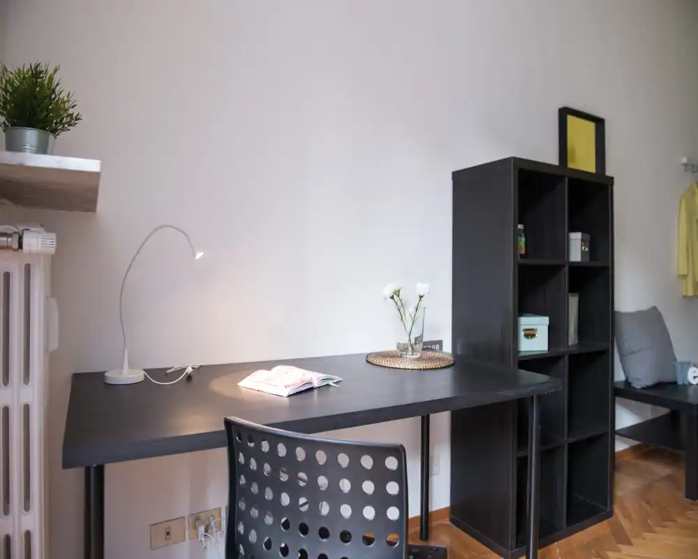 Espace de vie lumineux avec bureau noir et étagère modulable, chaise perforée, petites touches décoratives (plante et vase) et coin cosy — idéal pour travailler ou se détendre.