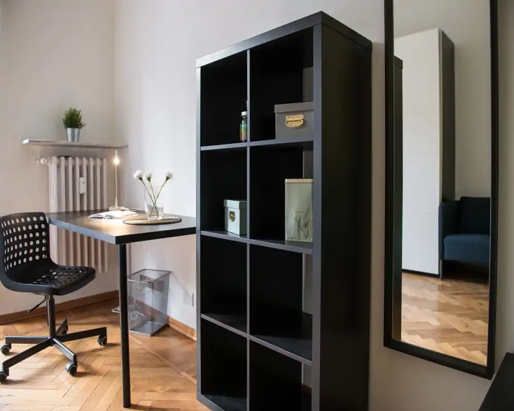 Coin séjour/travail moderne et lumineux avec bureau compact, chaise et étagère ouverte ; le parquet et le miroir donnent de l'espace et de la lumière.