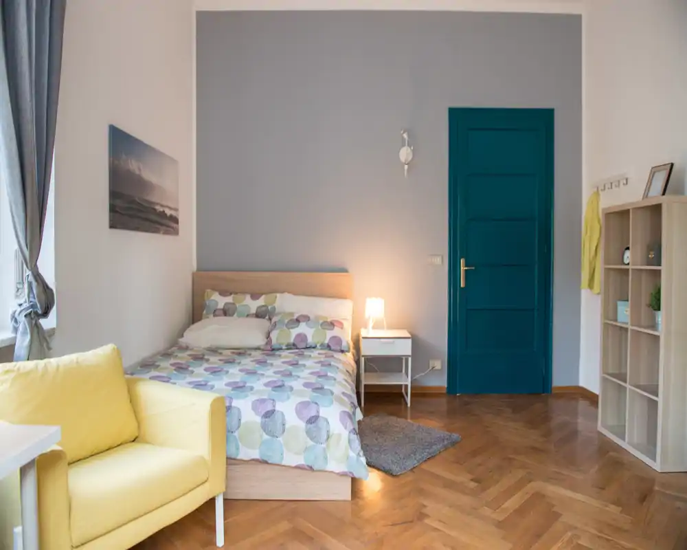Dormitorio luminoso y bien decorado con cama doble, mesita y lámpara acogedora; suelo de parquet y pared azul que aportan calidez.