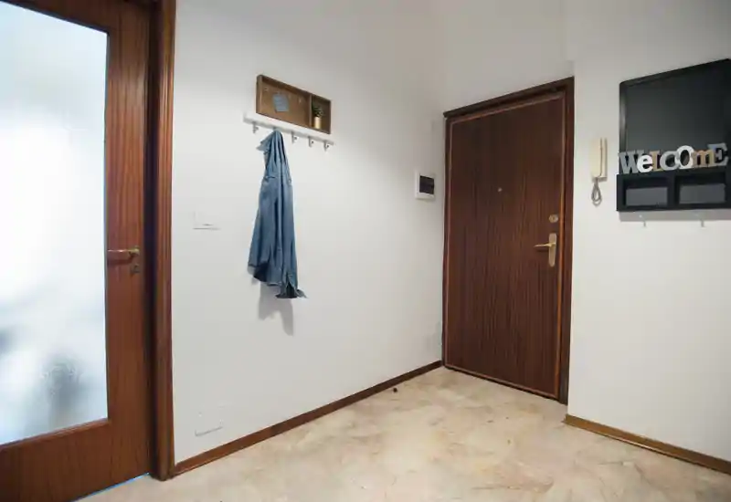 Bright, tidy entrance hallway with a wooden front door, coat hooks and a frosted glass interior door; clean marble floor and simple wall-mounted organizer welcome guests.
