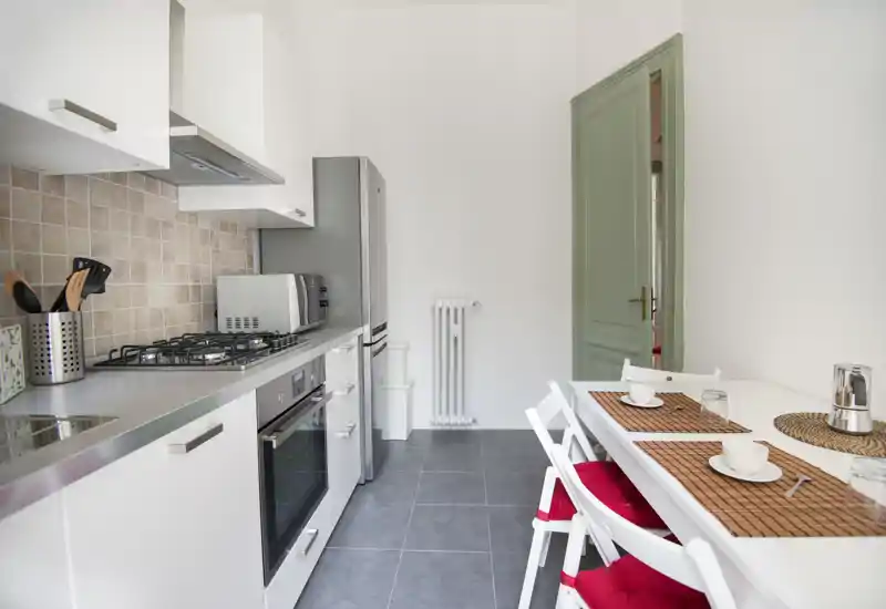 Bright, modern galley kitchen with stainless appliances, gas hob and a small dining area set with placemats and red-cushioned folding chairs.