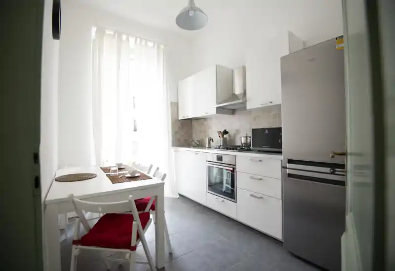Bright modern kitchen with white cabinets, stainless refrigerator and a small dining table — tidy, well-lit space ideal for short stays.