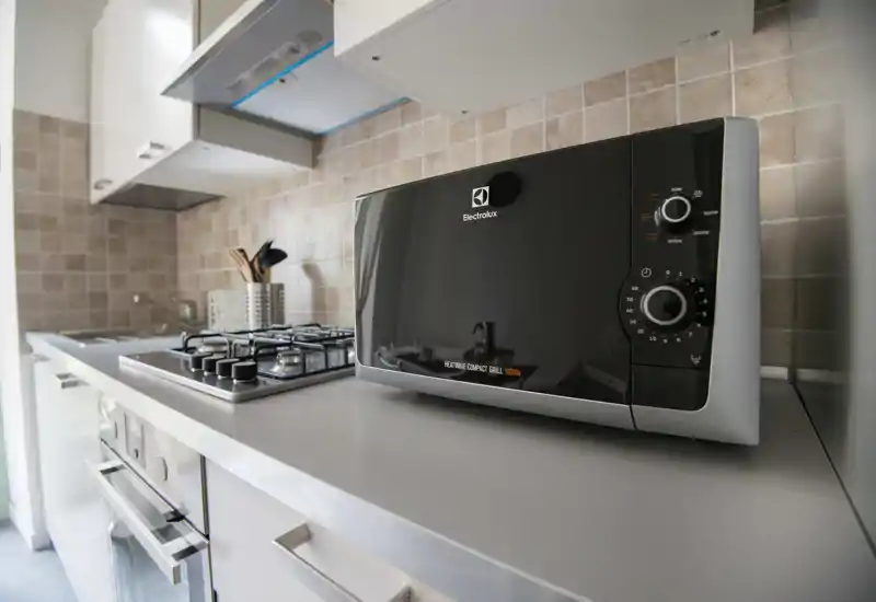Modern compact kitchen with stainless appliances, a gas hob and a black microwave on the counter. Clean, well-lit worktop ideal for short-stay rentals.