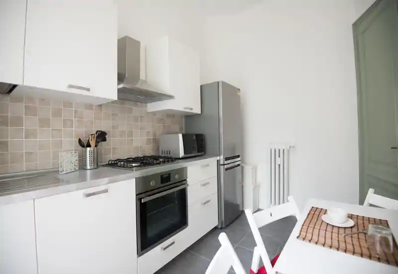 Modern, compact kitchen with white cabinets, stainless-steel appliances and a small dining area — bright and tidy, ideal for short-term rentals.