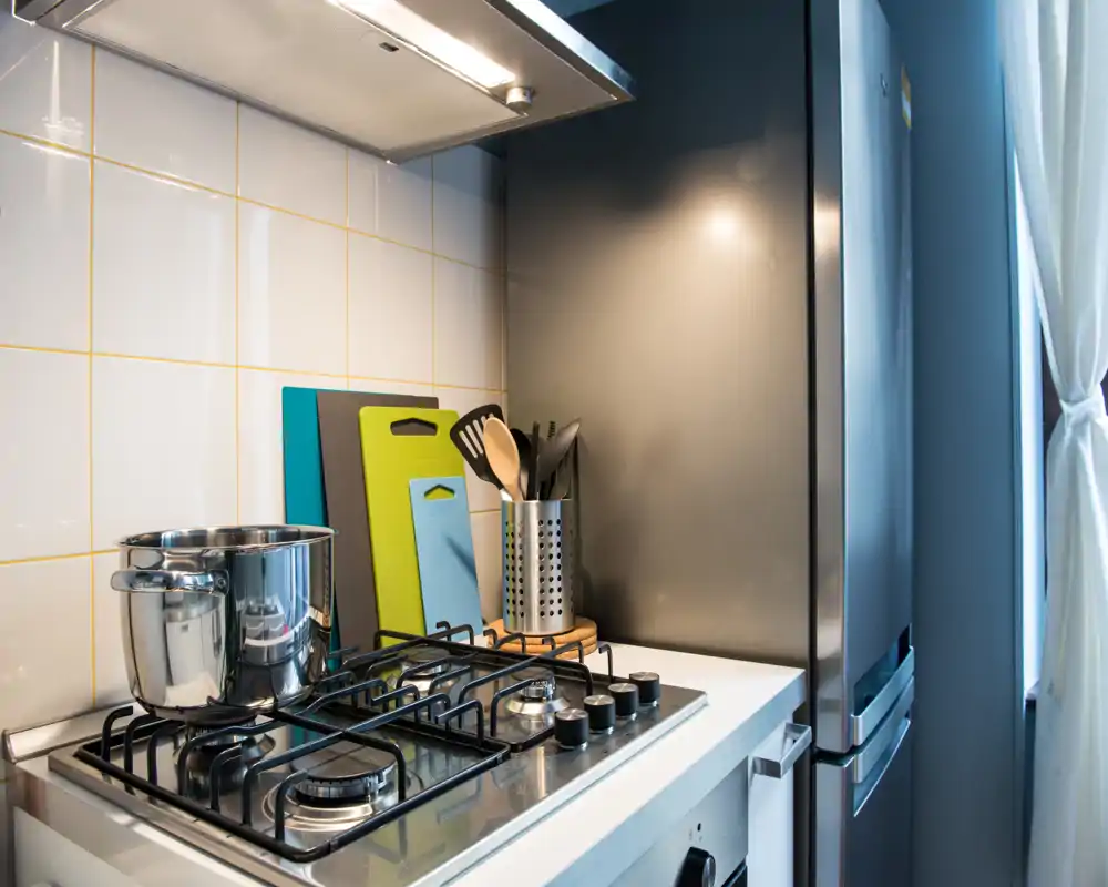 Rincón de cocina moderno con cocina de gas, cazo de acero, soporte de utensilios y frigorífico; luminoso y bien presentado para un anuncio.