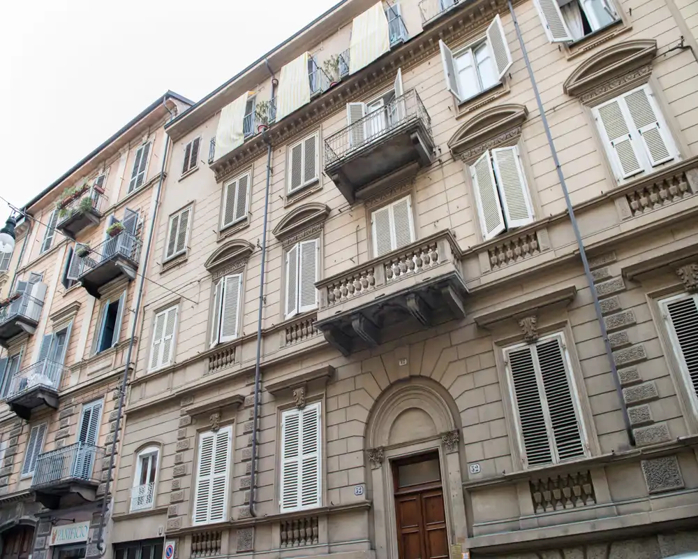 Vista exterior de la fachada de un edificio de varias plantas con balcones, persianas y puerta principal — adecuada como imagen exterior o de calle para un anuncio.