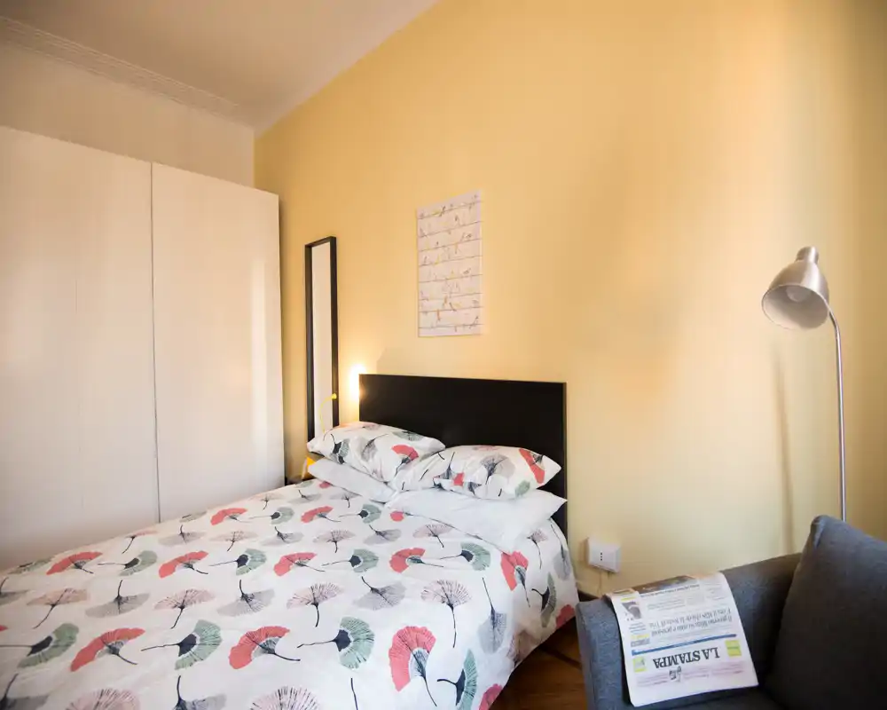 Bright, cozy bedroom with a double bed, patterned duvet, bedside lamp and a wardrobe — ideal for comfortable stays.