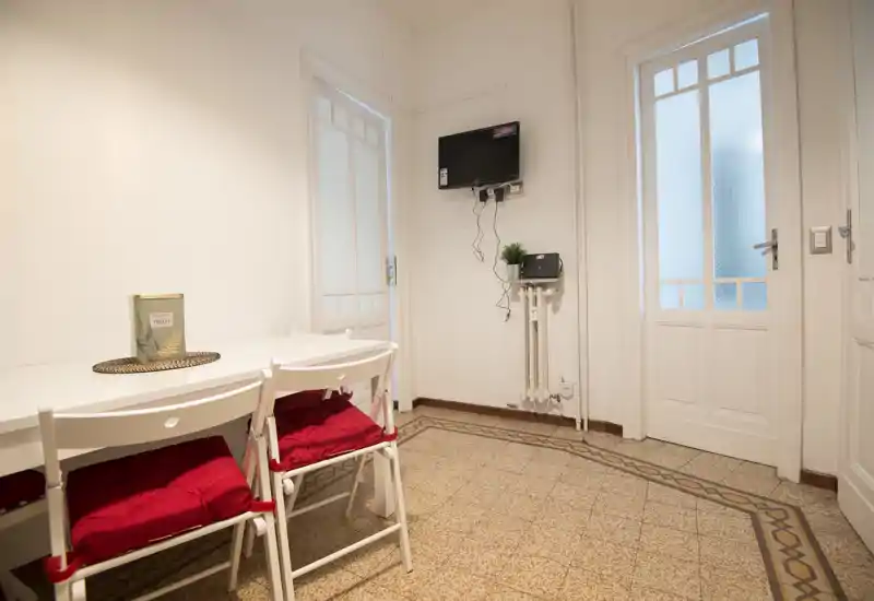 Compact dining area with a white table and folding chairs topped with red cushions, decorative centerpiece, patterned tile floor and two frosted glass doors—bright and neatly arranged for meals.