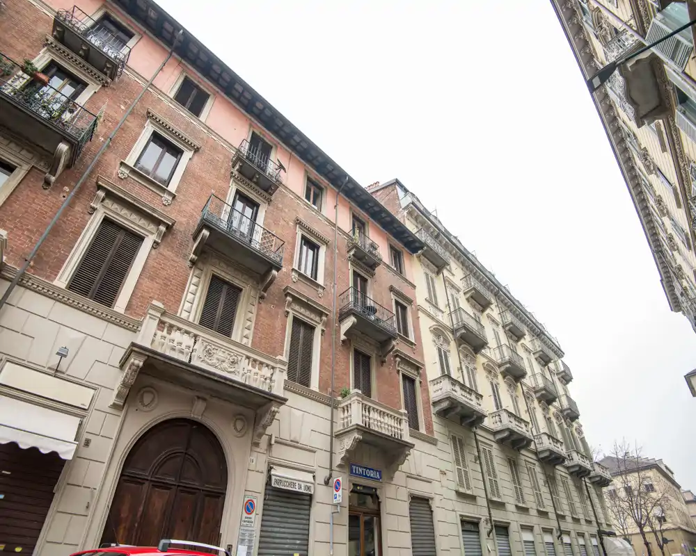 Facciata esterna di un edificio residenziale su strada con balconi e negozi al piano terra; vista esterna urbana, non una stanza interna.
