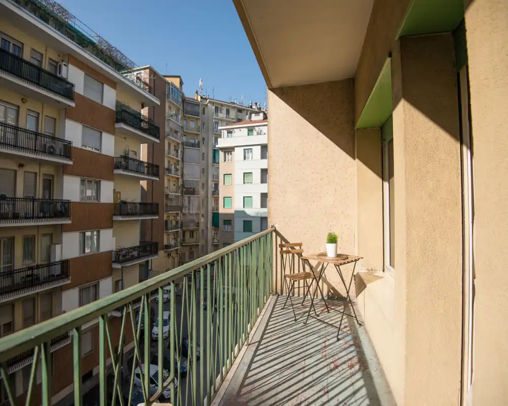 Balcón soleado con una pequeña mesa tipo bistró y dos sillas, vistas a la ciudad y luz natural cálida — ideal para el café de la mañana.