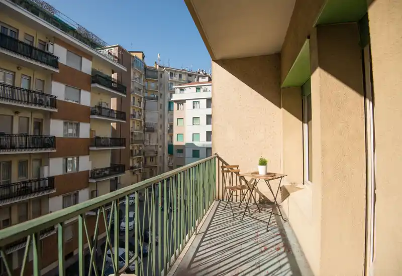 Balcone soleggiato con un piccolo tavolino e due sedie, vista sulla città e luce naturale calda — perfetto per il caffè del mattino.