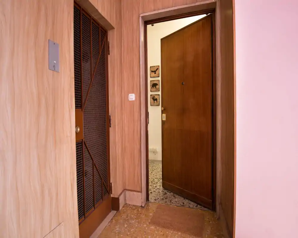 Entrada acogedora con puerta de madera entreabierta, suelo de baldosas y paredes revestidas en madera; ideal para mostrar la zona de acceso.
