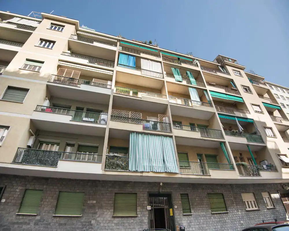 Vista exterior de un edificio residencial de altura media con balcones y toldos bajo un cielo azul despejado.