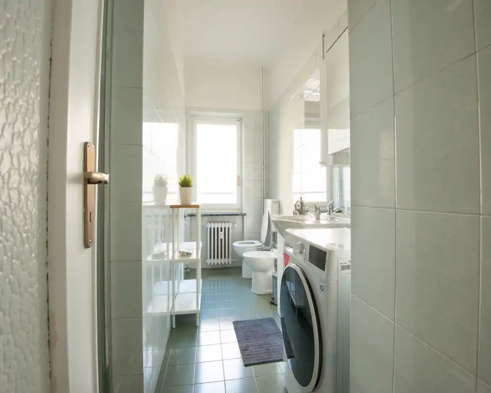 Baño luminoso y cuidado con lavadora, bidé, inodoro y lavabo doble; la ventana ofrece luz natural y ventilación.