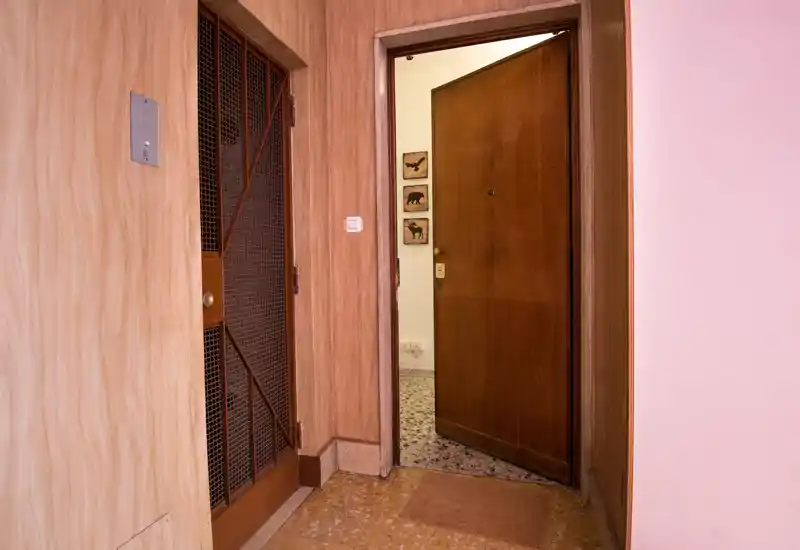 Ingresso con porta d'ingresso in legno leggermente aperta, pavimento piastrellato e pareti rivestite in legno; ideale per mostrare l'area d'entrata dell'abitazione.