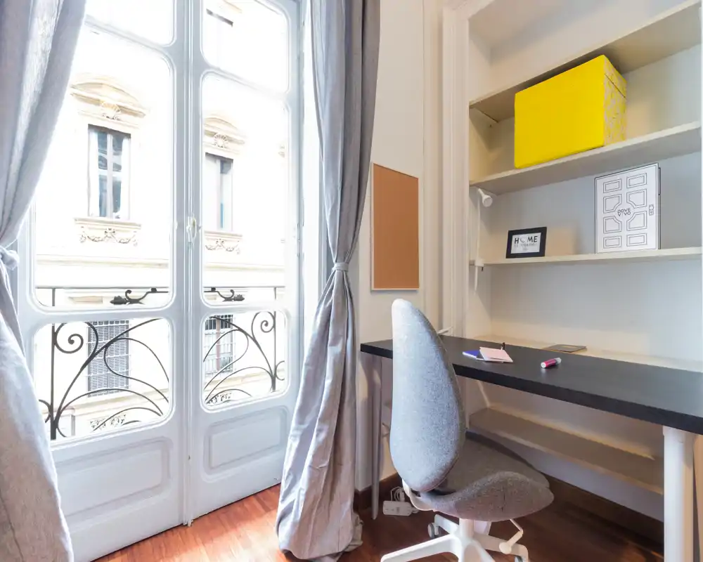 Coin bureau lumineux avec une grande fenêtre de style français, bureau, étagères et chaise confortable — idéal pour le télétravail avec beaucoup de lumière naturelle.