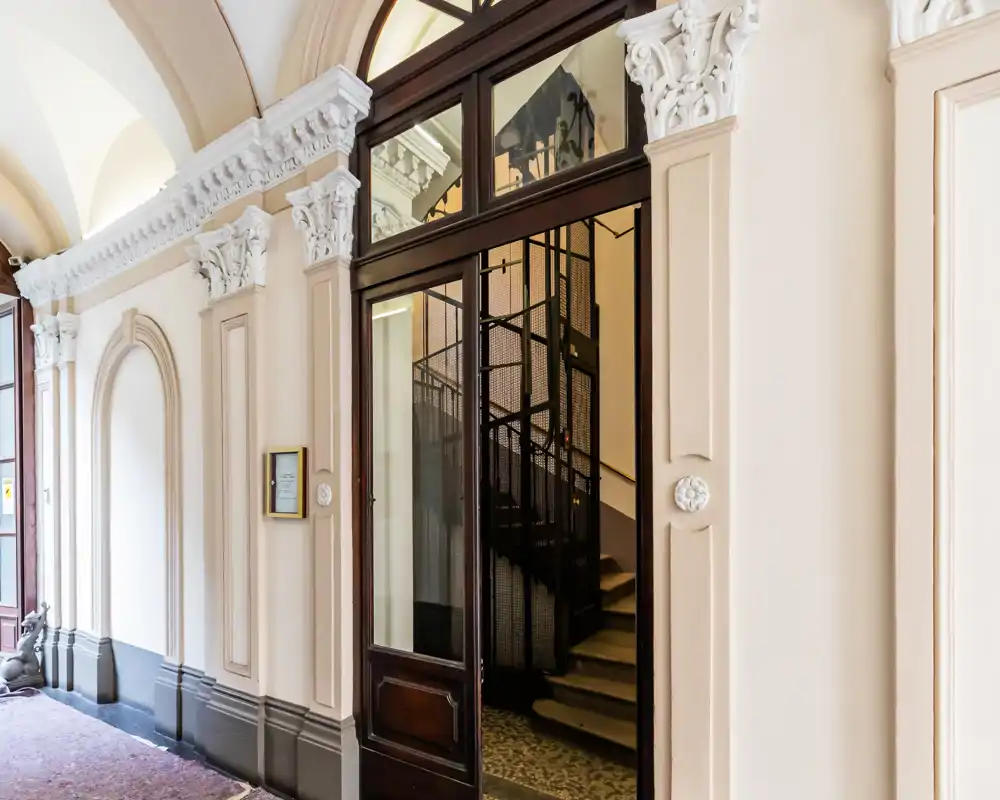 Entrée d'immeuble lumineuse et ornée avec moulures décoratives, plafond voûté et porte vitrée laissant apercevoir l'escalier/ascenseur. Photo détaillée idéale pour valoriser l'espace d'accueil commun.