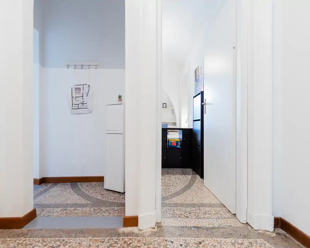 Entrée/couloir lumineux et soigné avec un sol en terrazzo décoratif, murs blancs et lignes modernes ; un petit meuble de rangement et une porte ouverte laissent voir une pièce adjacente.