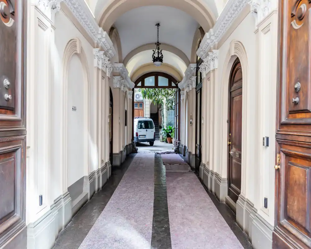Hall d'entrée orné avec voûtes hautes, moulures décoratives et tapis menant à une cour intérieure — espace lumineux et symétrique idéal pour présenter un bel accès d'immeuble.