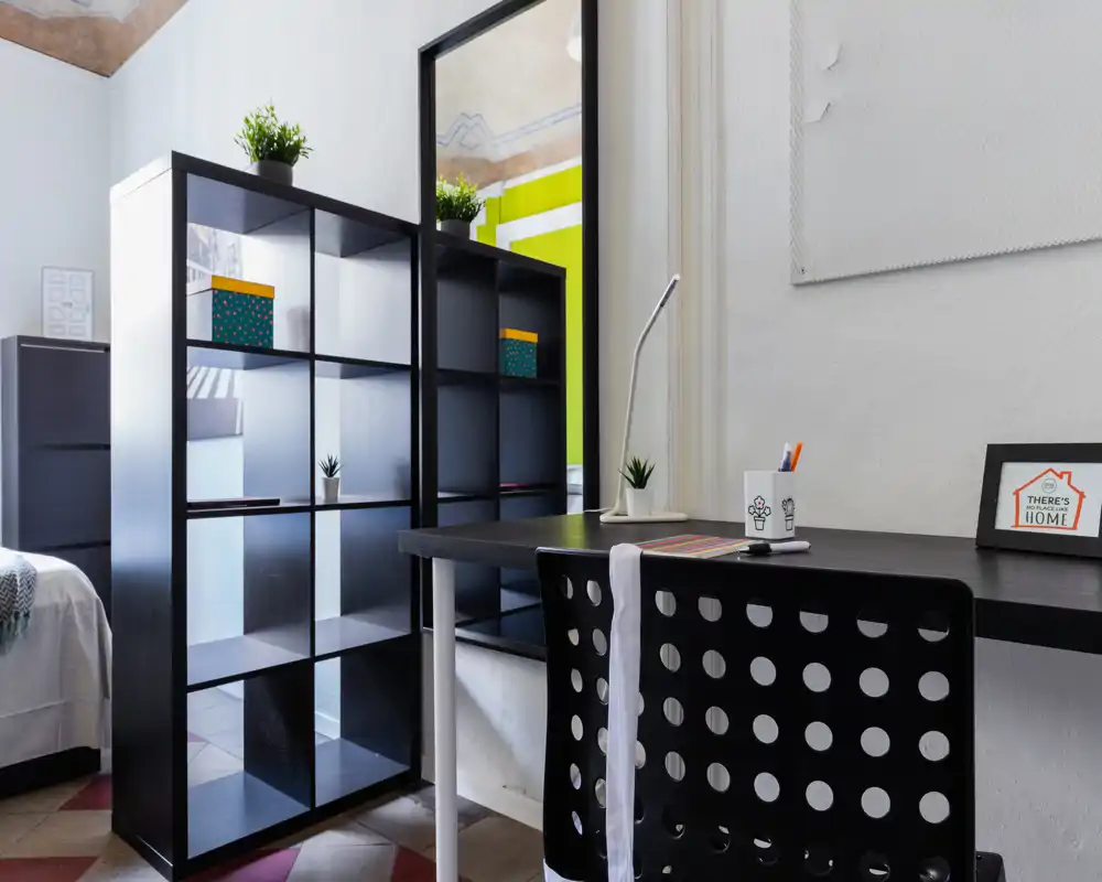Angolo camera da letto moderno con letto visibile, scaffalatura aperta e scrivania ordinata — luminoso, minimale e ben organizzato per studiare o rilassarsi.