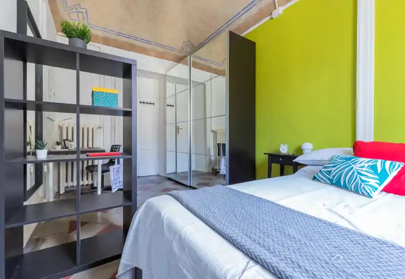 Camera da letto moderna e luminosa con letto ben rifatto, cuscini colorati e un armadio con ante a specchio che ampliano visivamente lo spazio.