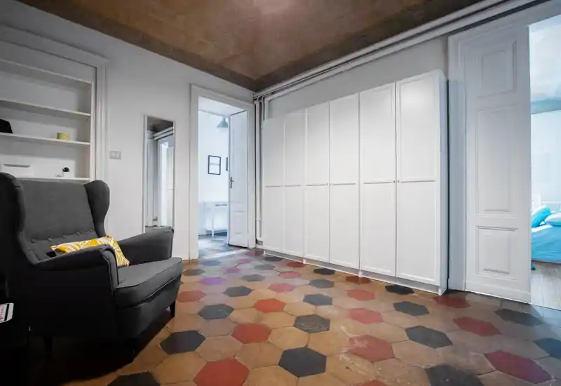 Zona giorno luminosa e di stile con una comoda poltrona, scaffalature integrate e grandi armadi: il pavimento esagonale decorato e i soffitti alti danno carattere.