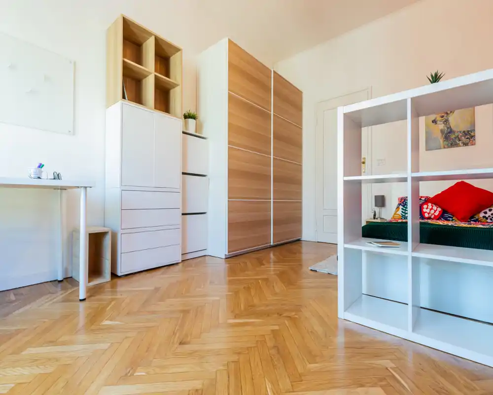 Chambre lumineuse et moderne avec parquet, placards intégrés et lit partiellement visible avec coussins colorés ; décor propre, aéré et bien mis en valeur pour une annonce.