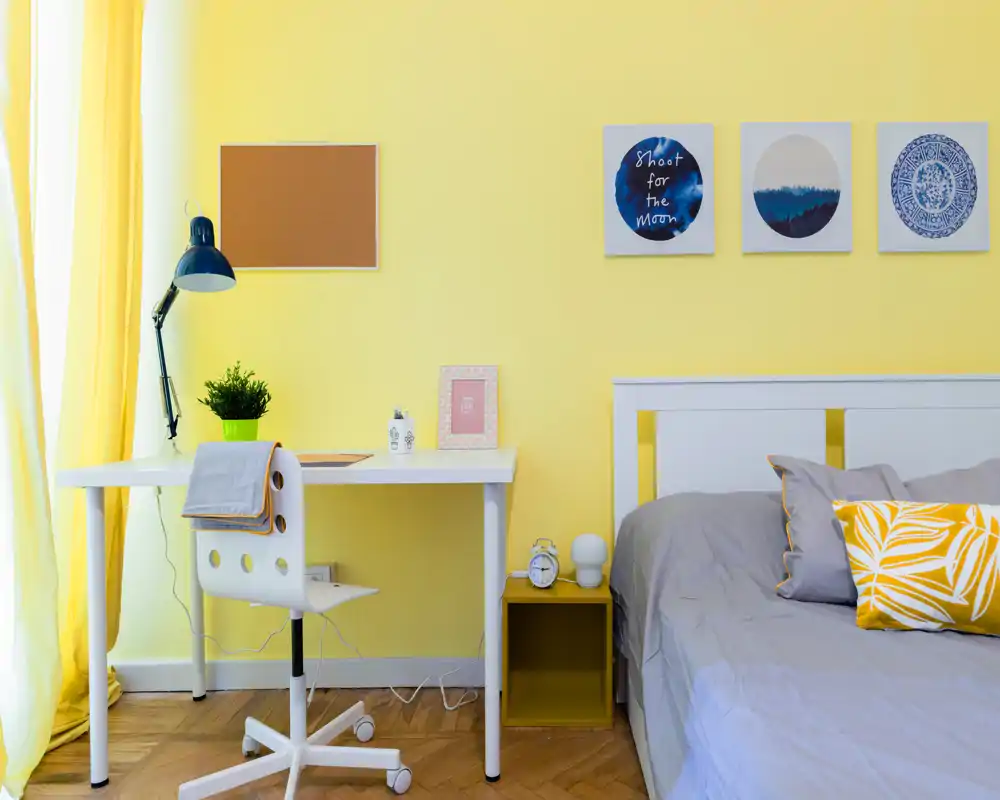 Rincón de dormitorio moderno y luminoso con cama blanca y ropa de cama gris, una mesita y un escritorio blanco junto a la ventana — brillante, acogedor y bien presentado para anuncios.