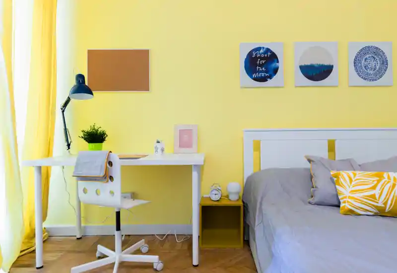 Rincón de dormitorio moderno y luminoso con cama blanca y ropa de cama gris, una mesita y un escritorio blanco junto a la ventana — brillante, acogedor y bien presentado para anuncios.