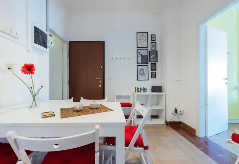 Bright, modern dining area with a white table, red cushioned folding chairs and simple decorative accents creating a welcoming eating space.