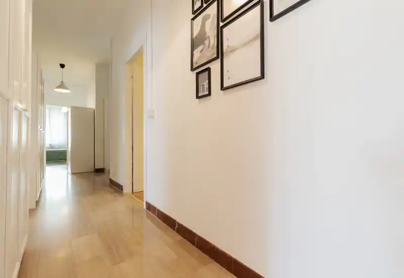 Bright, clean hallway with glossy wooden floor, white walls and framed artwork — a clear entrance/corridor leading to inner rooms.