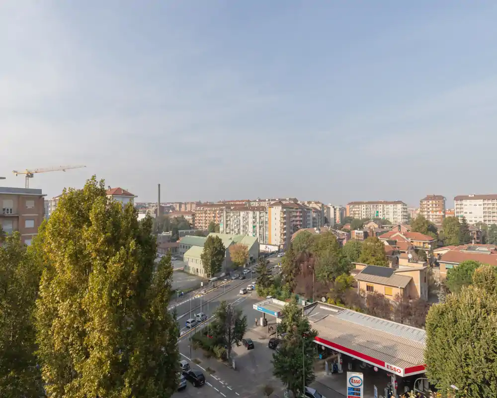 Veduta cittadina da un punto esterno elevato che mostra palazzi residenziali, strade alberate e una stazione di servizio in primo piano—luce diurna e buona visibilità, utile per descrivere il quartiere.