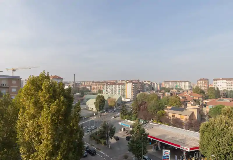 Cityscape view from an elevated outdoor vantage point showing residential blocks, tree-lined streets and a gas station in the foreground—bright daylight and clear visibility, ideal for highlighting the neighbourhood.