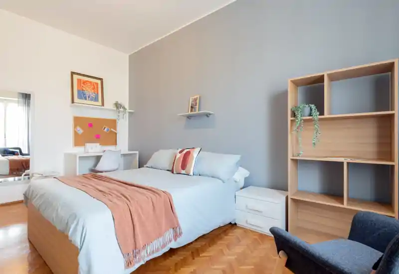 Bright, stylish bedroom with a neatly made double bed, decorative cushions and a warm throw; desk and shelving create a functional, comfortable space.