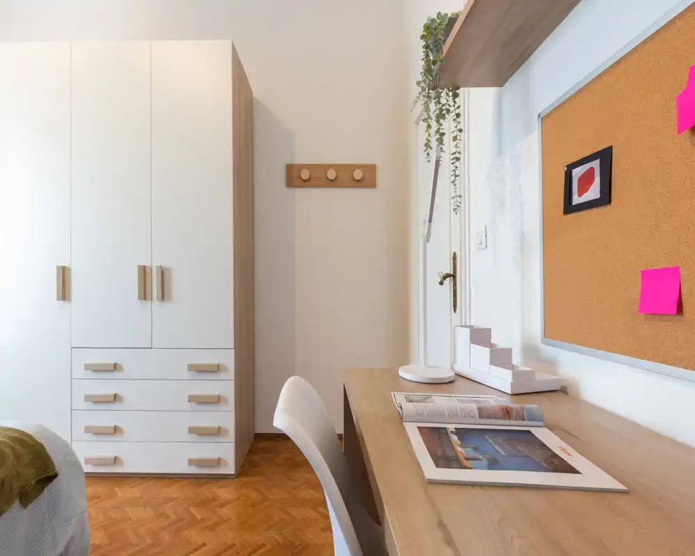 Angolo camera luminoso e ben arredato con scrivania in legno, armadio e vista parziale del letto — ideale per chi cerca uno spazio per lavorare e riposare.